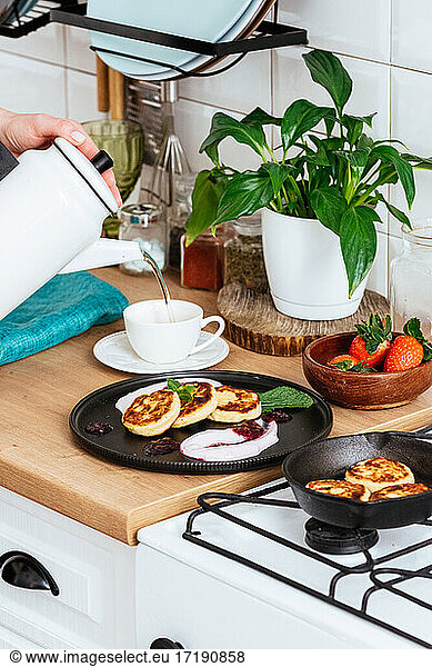 Women's hands pour tea into a cup. cheese pancakes with jam on a