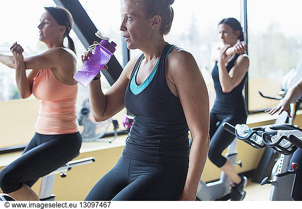 Women stretching hands while sitting on exercise bikes in gym