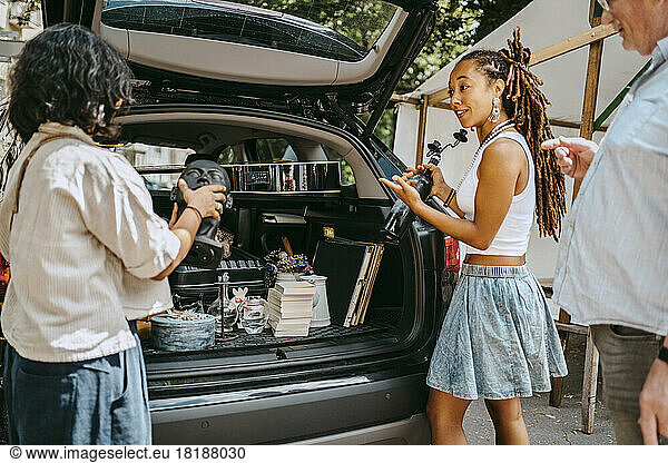 Women talking to each other while loading merchandise in car trunk at flea market