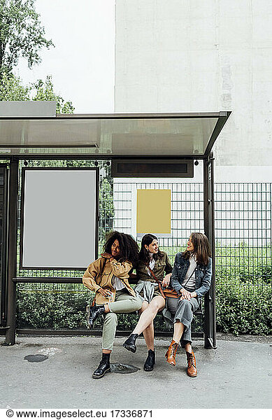 Women talking while sitting at bus stop
