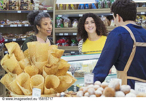Women talking with worker at bakery display case in supermarket