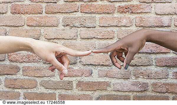 Women touching index fingers by brick wall