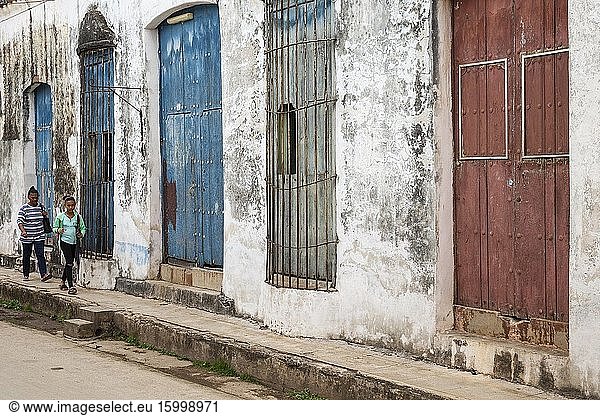 Women walking past decayed fa?ades of crumbling plaster and weathered wooden doors. Remedios  Cuba.