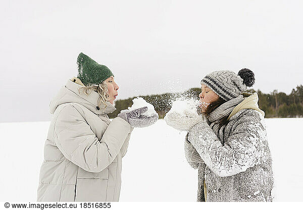 Women wearing knit hats blowing snow at each other
