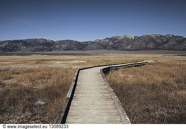 Wooden boardwalk on grassy field against mountains at Mammoth Lake Hot Springs