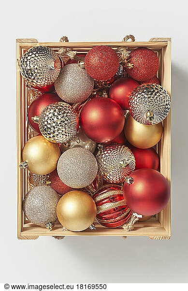 Wooden box with shiny christmas baubles against white background