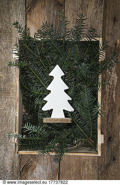 Wooden Christmas tree decoration lying in crate filled with conifer twigs
