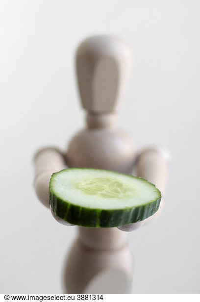 Wooden doll with a slice of cucumber,  symbolic image for healthy food