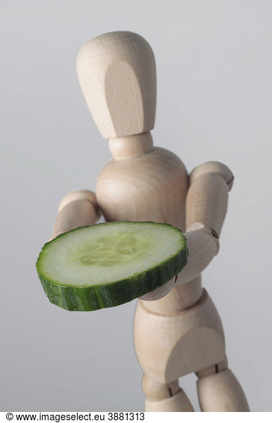 Wooden doll with a slice of cucumber  symbolic image for healthy food