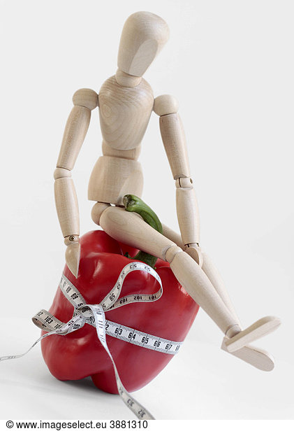 Wooden doll with red bell pepper and tape measure  symbolic image for healthy food or weight loss obsessions