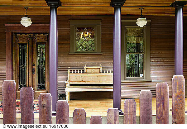 Wooden fence and house porch with columns and bench.