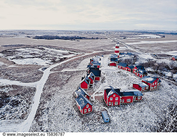 Wooden red houses of fishing village in snowy covered in winter. Stylish and modern fishing village from a bird's eye view. A few red houses near the lighthouse on the hill.
