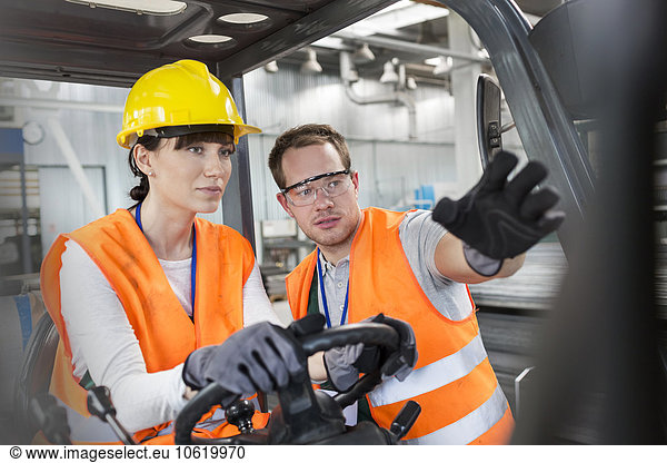 Worker guiding coworker driving forklift in factory