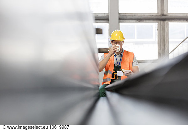 Worker in protective workwear drinking coffee in factory