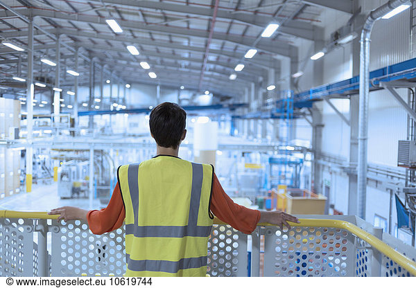 Worker in reflective clothing on platform looking out over factory