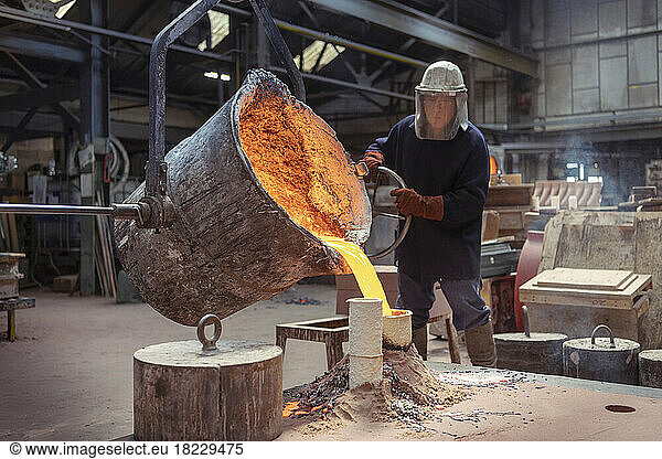 Worker pouring molten brass into large mold in brass foundry