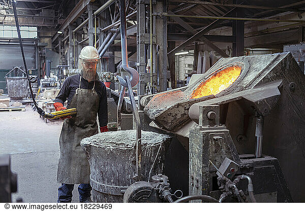 Worker preparing furnace full of molten brass in brass foundry