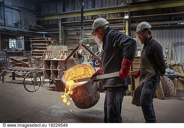 Worker skimming top of ladle of molten brass in brass foundry