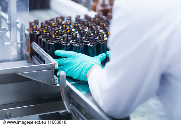 Workers arranging bottles on conveyor belt on production line in pharmaceutical plant  mid section