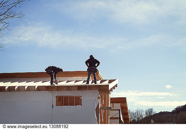 Workers constructing house roof against sky during sunny day