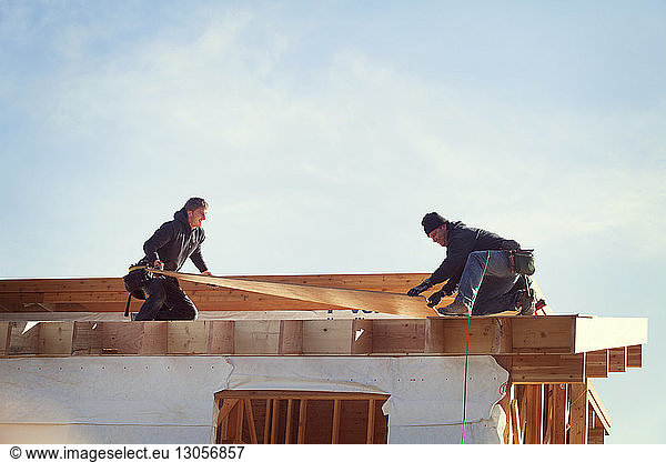 Workers constructing roof beam against sky during sunny day