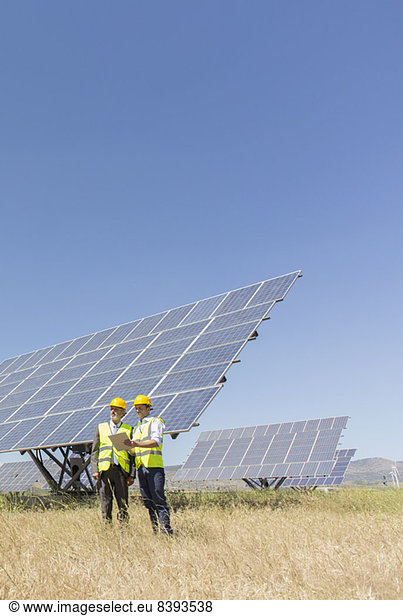 Workers standing by solar panels in rural landscape