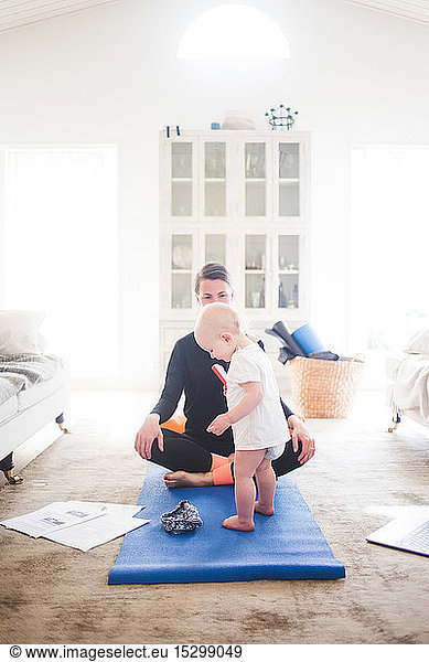 Working mother practicing yoga while daughter standing on exercise mat at home