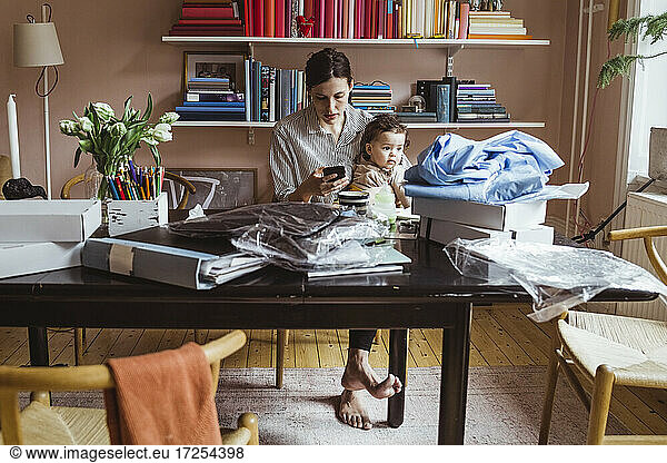 Working mother using smart phone while sitting with baby boy at home office
