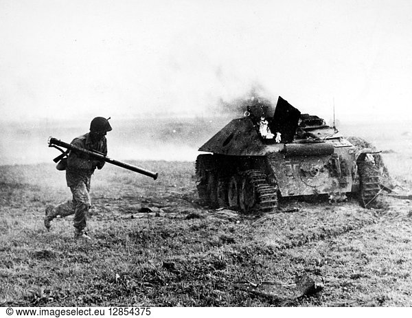 WORLD WAR II: ALDENHOVEN. American soldier of the 9th Army with a bazooka runs past a burning German tank destroyer near Aldenhoven, Germany. Photographed December 1944.