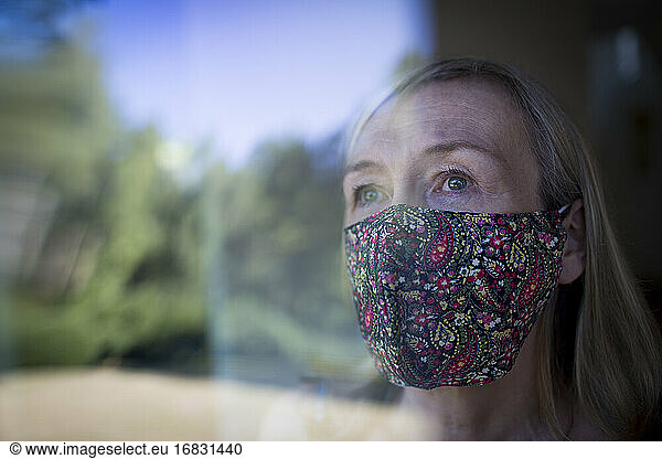 Worried senior woman in face mask at window