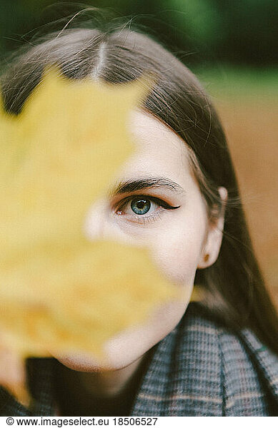 yellow autumn leaf covers the face of a young woman in autumn
