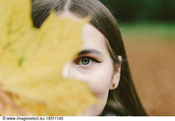 yellow autumn leaf covers the face of a young woman in autumn