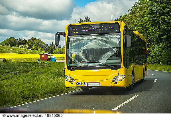 Yellow bus moving on road near grass