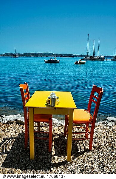 Yellow cafe restaurant table of street cafe with chairs on beach in Adamantas town on Milos island with Aegean sea with boats and yachts in background. Milos island  Greece