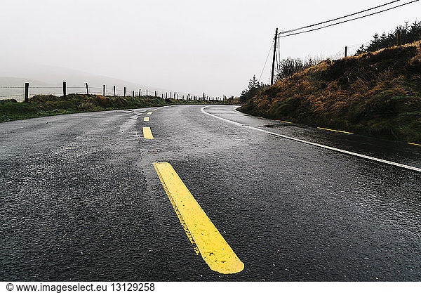 Yellow dividing lines on empty road against sky
