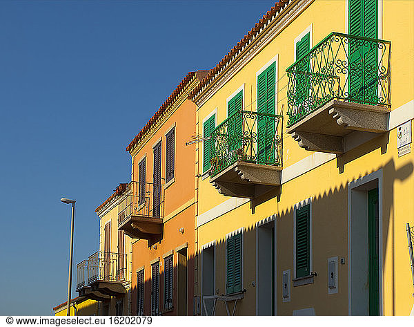 Yellow house facade with balconies and green window shutters  Sardinia  Italy