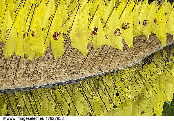 Yellow prayer flags stuck in sand over reflecting water at a wat temple.