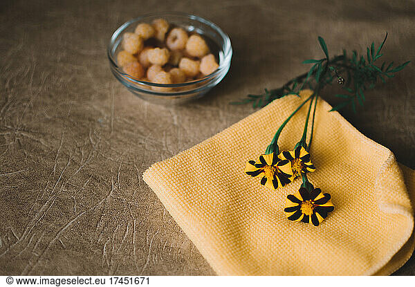 Yellow raspberries in glass plate and marigolds on napkin