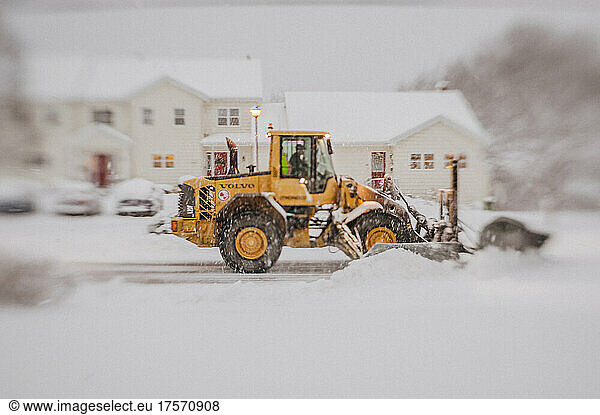 Yellow volvo grader plows road in blizzard