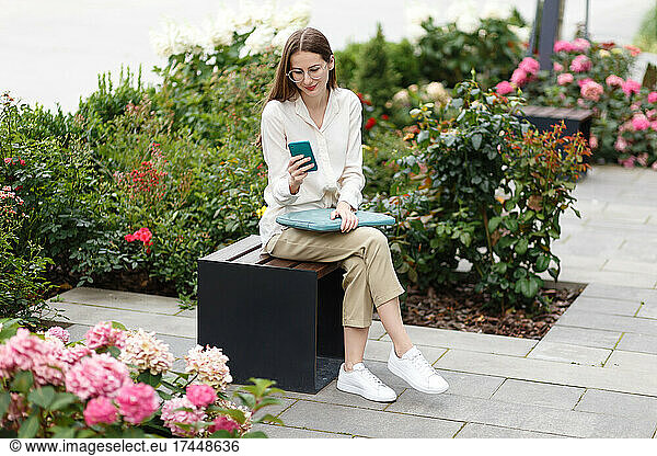 yong women with laptop using mobile phone while sitting