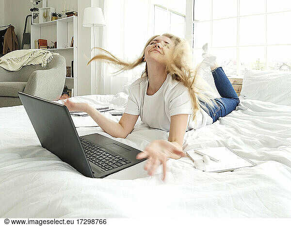 younf female plays with long blond hair lying on the bed with laptop