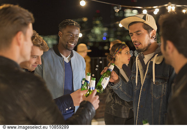 Young adult friends toasting beer bottles at rooftop party