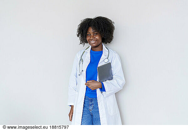 Young Afro doctor with tablet PC standing against white background