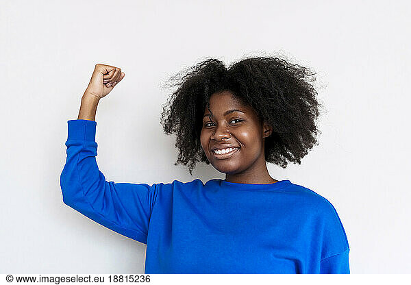 Young Afro woman flexing muscles against white background