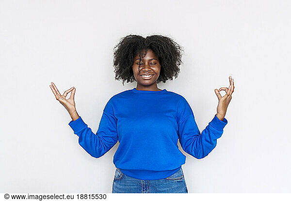 Young Afro woman gesturing mudra and meditating against white background