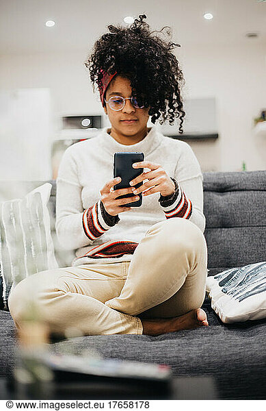 young Afro woman using her cell phone in comfort of her home