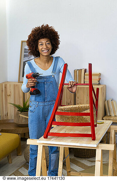 Young Afro woman with electric screwdriver repairing chair at home