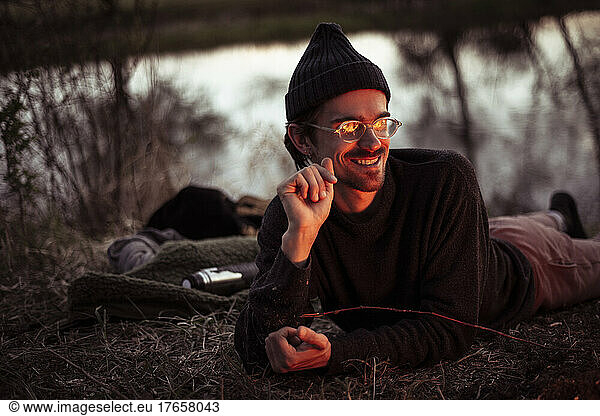 young alternative man with glasses relaxes by fire and water
