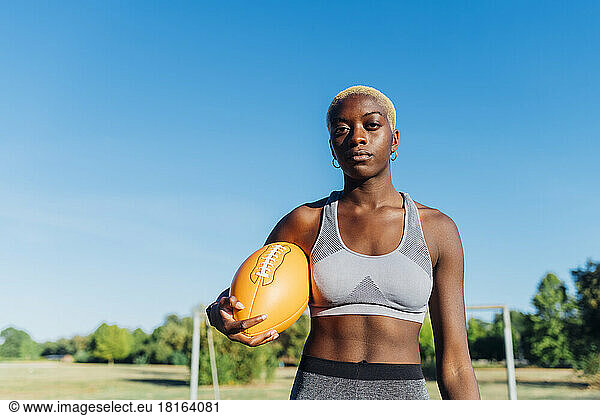 Young American football player with ball on sunny day