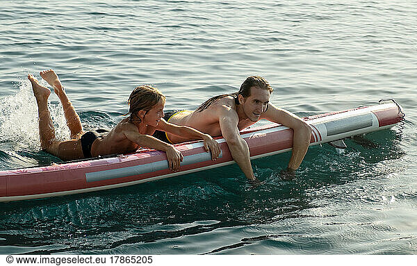 Young and older brothers swimming on SUP board in sea.